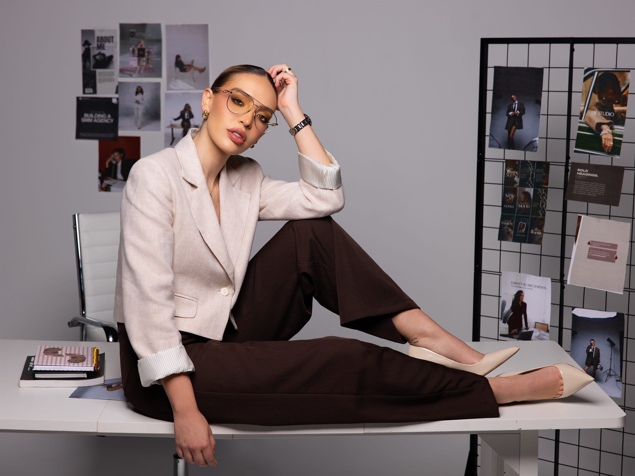 Laura Rentería seated on a studio desk amid moodboards, looking to camera.